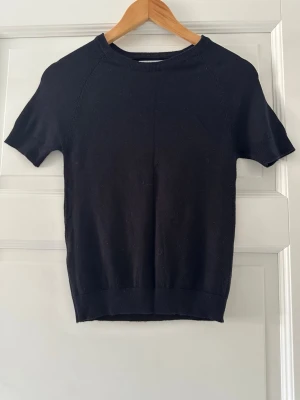 Svart kortärmad topp från MNG - En stilren svart topp från MNG med rund hals och korta ärmar. Toppen har en enkel, klassisk design och är tillverkad i ett mjukt stickat material som sitter snyggt på kroppen. Perfekt att matcha med jeans eller kjol för en clean look.