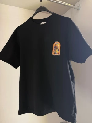 Svart Casa Blanca t-shirt med tryck - Snygg svart t-shirt från Casa Blanca med färgstarkt tryck av en stadsvy på bröstet och ryggen. T-shirten har rund hals, korta ärmar och är gjord i mjuk bomull. Perfekt för dig som vill ha en unik och trendig look. Alla storlekar finns