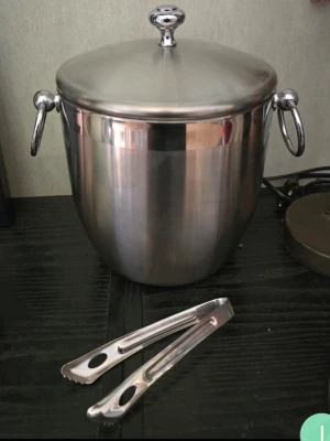 Isbehållare i rostfritt stål med tång ( oanvänd) - Säljer en stilren isbehållare i rostfritt stål med lock, handtag på sidorna och tillhörande istång. Behållaren har även ett insatslock med flera hål för enkel servering av isbitar. Perfekt till festen eller hemmabaren.