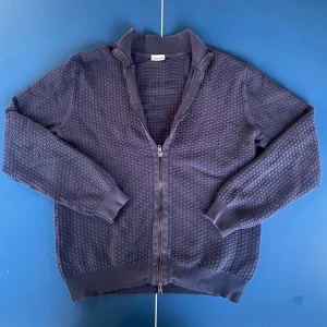 John Henric fullzip  - Snygg mörkblå ziptröja från John Henric med strukturerad stickning. Tröjan har hög krage, dragkedja framtill och ribbade muddar vid ärmslut och nederkant. Perfekt för lager på lager och enkel att matcha med olika outfits.