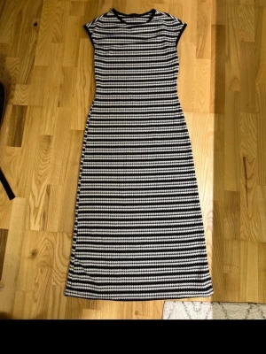 Svartvit långklänning med mönster - Snygg långklänning i svart och vitt med horisontella ränder. Klänningen har rund halsringning och är ärmlös, vilket ger en stilren och modern look. Perfekt för dig som gillar klassiska färger och mönster.