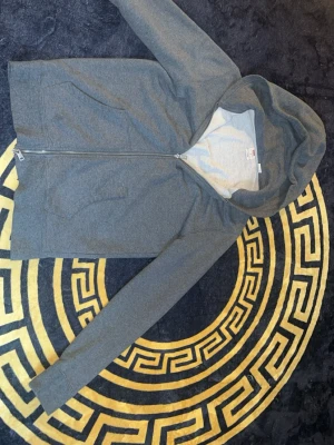Grå hoodie från Levi's med dragkedja - Säljer en stilren grå hoodie från Levi's i storlek S. Hoodien har dragkedja framtill, två fickor och en klassisk huva. Tillverkad i mjukt bomullsmaterial som känns skönt mot huden. Perfekt för en avslappnad och enkel look.