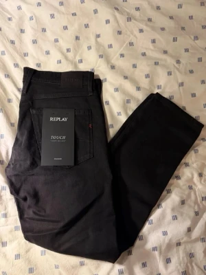 Svarta Replay jeans slim fit - Snygga svarta jeans från Replay i slim fit-modell. Jeansen har klassisk femficksdesign, normal midja och är tillverkade i ett mjukt stretchigt material för extra komfort. Perfekta för dig som gillar en stilren och modern look.