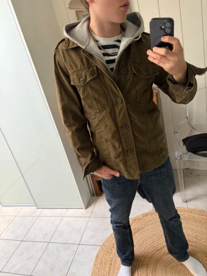 Overshirt från Abercrombie & Fitch - Säljer en olivgrön overshirt med klassisk krage och stora bröstfickor. Jackan har knappar framtill och är tillverkad i ett slitstarkt bomullstyg. Perfekt för lager på lager och har en avslappnad, loose passform. Är i storlek S men passar mig som är 185 cm och 75kg