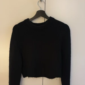 Svart croppad stickad tröja - Säljer en svart, croppad stickad tröja med lång ärm och rund hals. Brukar styla den med antingen en vit tshirt under eller ett spets linne för att spicea upp looken. Passar utmärkt både till jeans och till kjol.  
