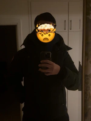Svart vinterjacka med hög krage - Säljer en svart vinterjacka med hög krage och breda kanaler. Jackan har en klassisk passform och ser riktigt varm ut, perfekt för kalla vinterdagar. Stängs med dragkedja och har diskret logga på ärmen. Obs! har ett litet håll man inte märker!