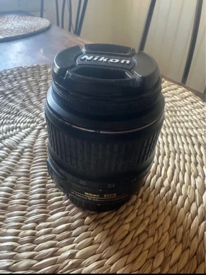 Nikon DX AF-S 18-55mm objektiv - Säljer ett svart Nikon DX AF-S Nikkor 18-55mm objektiv till kamera. Objektivet har zoomring och fokusring, samt lock med Nikon-logga. Passar till Nikon-systemkameror och är tillverkat i plast och glas. 