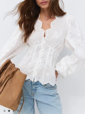 Vit broderad blus med puffärm - Romantisk vit blus med broderade blommor, v-ringad hals och dekorativa knappar framtill. Blusen har långa puffärmar och vågig kant nertill och vid halsen. Tillverkad i luftig bomull med hålbroderier som ger en bohemisk känsla.