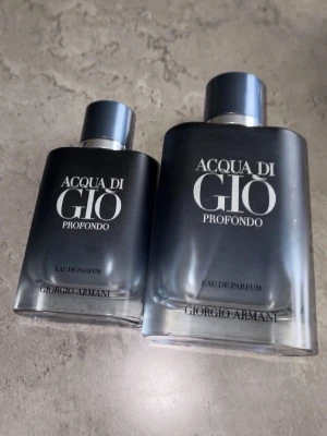 Acqua di Giò Profondo Eau de Parfum - Två tomma flaskor Acqua di Giò Profondo Eau de Parfum från Giorgio Armani. Flaskorna är mörkblå med silverfärgade lock och har en stilren, matt finish. Doften är fräsch och modern, perfekt för dig som gillar exklusiva parfymer med marint tema.