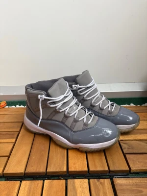 Gråa höga sneakers med vita snören - Snygga höga sneakers i olika grå nyanser med vita snören och vit sula. Ovandelen är i en mix av glansigt och matt material, vilket ger en modern look. Perfekta för dig som vill sticka ut med stilrena detaljer och sportig känsla.