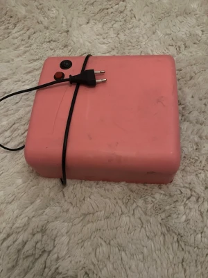 Rosa UV-lampa för naglar - En rosa UV-lampa för naglar med sladd och strömbrytare. Perfekt för att härda gelélack hemma. Lampan har en rektangulär form och är tillverkad i plast. Enkel att använda för snygga naglar.
