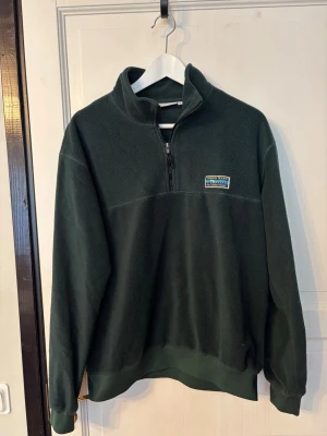 Junkyark fleece (S) - Mysig mörkgrön fleece med halv dragkedja och hög krage. Urban Tears-märke på bröstet. Perfekt för lager-på-lager och chill dagar. Tillverkad i mjukt fleecematerial som håller dig varm. Långärmad och med ribbade muddar vid ärmslut och nederkant.