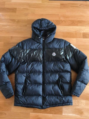 Svart Moncler jacka - Tvär fet Moncler jacka som värmer och hettar upp din outfit. Jackan är välgjord som gör den riktigt skön att ha på sig, samt sköna fickor. Loggan ser också äkta ut. Dragkedjan på fickorna och till jackan har också Moncler märket på sig 
