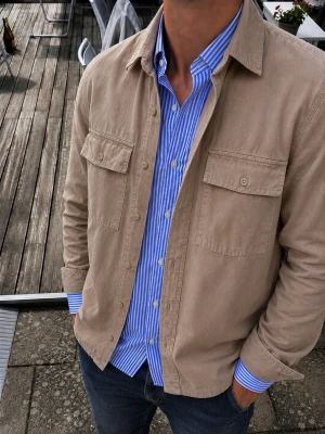 Samsøe Samsøe Overshirt Beige/Taupe – Storlek S - Snygg och stilren overshirt från Samsøe Samsøe i en beige/taupe nyans. Tillverkad i ett kraftigare tyg med fin struktur och flera praktiska fickor framtill. Klassisk skjortkrage, knappstängning och avslappnad men stilren passform. Storlek S. Perfekt att bära över skjorta, T-shirt eller stickat.