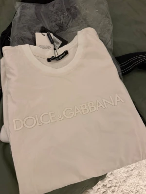 Vit Dolce & Gabbana t-shirt - Snygg vit t-shirt från Dolce & Gabbana med diskret logotyp i relief framtill. Klassisk rund halsringning och korta ärmar. Tillverkad i mjuk bomull för en skön känsla och stilren look. Den passar mer som M!!