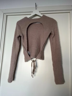 Beige fluffig cardigan med öppen rygg  - Supersöt beige cardigan i fluffigt material med långa ärmar och knytband framtill. Öppen i ryggen. Perfekt att slänga över ett linne eller topp för en mysig och trendig look. 