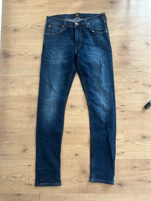 Mörkblå jeans från Lee - Snygga mörkblå jeans från Lee med klassisk femficksdesign och raka ben. Jeansen har kontrastsömmar och en diskret tvättad look som ger en cool vibe. Tillverkade i slitstarkt denimtyg som passar perfekt till din vardagsstil.