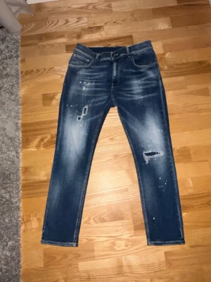 Dondup Alexs Jeans - Säljer ett par blå jeans från Dondup med slitningar och distressed detaljer på både fram- och baksida. Jeansen har klassisk femficksmodell, normal midja och raka ben. Materialet är denim i bomull med cool tvätt och färgstänk för en trendig look. Helt nya 