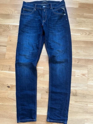 Mörkblå raka jeans från Replay - Snygga mörkblå jeans från Replay med raka ben och klassisk femficksmodell. Jeansen har kontrastsömmar och detaljerade bakfickor. Materialet är denim med en lätt stretch för extra komfort. Perfekta för en avslappnad och stilren look.