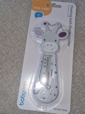 Badtermometer - Söt flytande badtermometer i form av en giraff från babyono. Termometern är vit med lila och grå detaljer och har ett tydligt mätfönster för att enkelt läsa av vattentemperaturen. Perfekt för att hålla koll på badvattnet till de minsta.