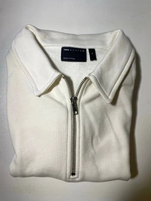 Vit tröja med halv dragkedja ASOS - Vit långärmad tröja från ASOS DESIGN med halv dragkedja och klassisk krage. Tröjan har ribbade muddar och är tillverkad i ett mjukt material som känns skönt mot huden. Perfekt för en clean och stilren look.
