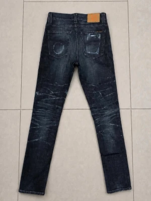 Nudie Jeans 30/34 - Snygga mörkblå jeans i slim fit-modell med tydliga slitningar och tvättade detaljer på både fram- och baksida. Klassisk femficksdesign och raka ben. Perfekta för en trendig och avslappnad stil.