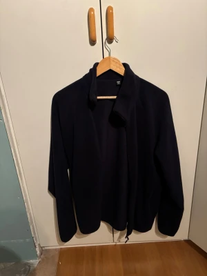 Mörkblå fleecekofta med hög krage - Mysig mörkblå fleecekofta med hög krage och dragkedja. Koftan har en enkel och stilren design med långa ärmar och mjukt material som passar perfekt för kyliga dagar nu i höst. Flisen är från uniqlo och är i storlek M
