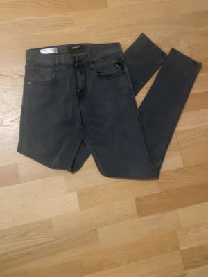 Mörkgrå replay slim fit jeans - 30/34 Snygga mörkgrå slim fit jeans med klassisk femficksdesign och svarta detaljer. Jeansen har raka ben och bälteshällor, samt dekorativa sömmar på bakfickorna. Perfekta för en avslappnad och trendig look.
