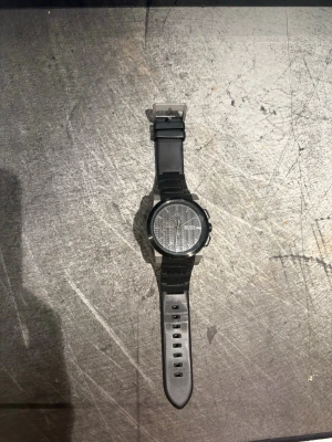 Svart klocka från Hugo Boss - Stilren svart klocka från Hugo Boss med rund urtavla och svart silikonarmband. Klockan har diskreta detaljer och en modern look, perfekt för dig som gillar minimalistisk design. Vattentät upp till 50 meter och tillverkad i rostfritt stål.