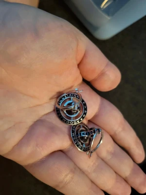 Vivienne Westwood x Nana örhängen - Säljer ett par ikoniska silvriga örhängen från Vivienne Westwood x nana med det klassiska orb-motivet. Örhängena har rund form med text runt kanten och hängsmycke. Perfekta för dig som gillar statement-smycken och vill sticka ut.