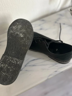 Svarta loafers med snörning - Stilrena svarta loafers med snörning och låg sula. Skorna har en klassisk form och är tillverkade i ett matt material som ser ut som mocka eller nubuck. Passar perfekt till både jeans och chinos för en clean look.
