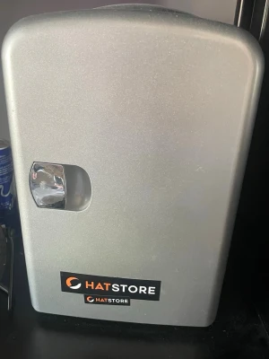 Silverfärgad minikyl med Hatstore-logga - Säljer en kompakt och stilren minikyl i silverfärg med Hatstore-logga på framsidan. Kylen har en blank handtag och rundade kanter, perfekt för att förvara drycker eller snacks nära till hands. Tillverkad i metall. Strömförsörjning 230 V AC eller 12 V DC, vilket gör den lika användbar i hemmet som i bilen, båten eller på campingen.