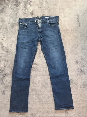 Replay Mörkblå slim fit jeans - Snygga mörkblå slim fit jeans från Replay med klassisk femficksdesign och dragkedjegylf. Jeansen har en stilren look med diskreta slitningar och är tillverkade i ett mjukt denimtyg som sitter skönt hela dagen.
