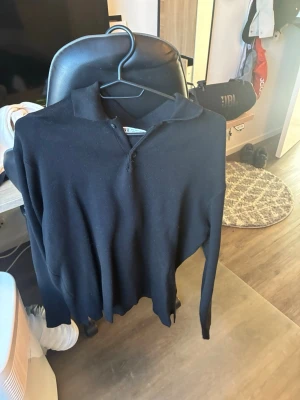 Svart pikétröja från Zara - Klassisk svart pikétröja från Zara med krage och knappar framtill. Tröjan har lång ärm och är tillverkad i ett mjukt material som känns skönt mot huden. Perfekt för en clean och stilren look.