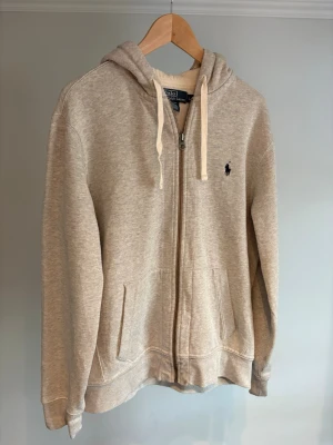 Polo Ralph Lauren zip hoodie  - Snygg grå hoodie med dragkedja från Polo Ralph Lauren. Klassisk design med huva och vita dragsnören, två fickor framtill och den ikoniska lilla loggan broderad på bröstet. Perfekt för en avslappnad och stilren look. Nypris ligger på runt 2500 kr. Personen på bild är 175 cm 