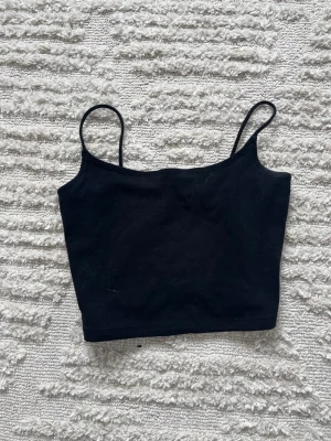 Svart croppad linnetopp - En enkel och stilren svart croppad linnetopp med smala axelband. Perfekt att matcha med höga jeans eller kjol för en trendig look. Mjuk och stretchig känsla, passar till många olika outfits.