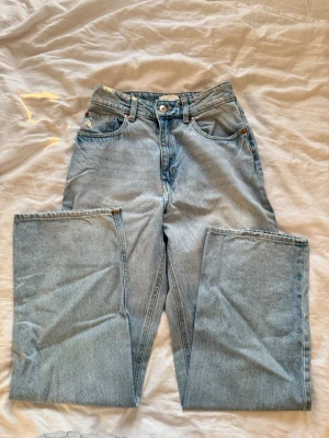 Ljusblå raka jeans med hög midja - Säljer ett par ljusblå jeans med rak passform och hög midja. Klassisk femficksmodell med knappgylf och bälteshällor. Jeansen har en vintagekänsla och är tillverkade i kraftig denim. Perfekta för en avslappnad och trendig look.