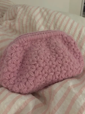 Rosa virkad väska - Superfin rosa virkad väska med clutch handtag! Perfekt för en extra touch i sin outfit! Väska är gjort med ett clutch handtag som är 20cm. Virkas efter beställning så det går att få vilken färg och stolek som helst. Går även att få med innertyg som ger extra stabilitet i botten! Priset är endast baserat på material som används och varierar därför efter önskemål om färg och stolek! 