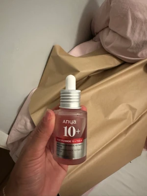 Anua Niacinamide 10+ serum - Säljer ett Anua 10+ Niacinamide serum med TXA4. Kommer i en frostad glasflaska med pipett och har en röd etikett. Perfekt för dig som vill boosta din hudvårdsrutin med niacinamid och tranexaminsyra.