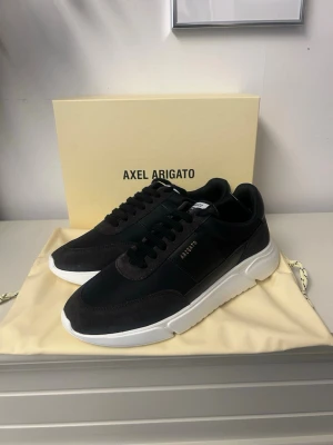 Svarta sneakers Axel Arigato - Stilrena svarta sneakers från Axel Arigato med ovandel i mocka och textil helt nya, samt vit chunky sula. Diskret logga i guld på sidan och klassisk snörning. Perfekta för en clean och modern look.