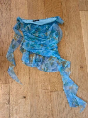 Blommig blå omlottopp från Zara - Säljer en superfin blommig omlottopp från Zara i blå och gröna toner. Toppen är ny utan prislapp och har meshigt material och volangdetaljer. Perfekt för dig som vill sticka ut med en unik och trendig topp!
