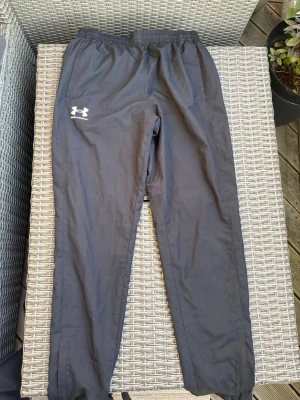 Svarta träningsbyxor Under Armour - Snygga svarta träningsbyxor från Under Armour med resår i midjan och vita loggan på vänster lår. Byxorna har raka ben och sidofickor, perfekta för gymmet eller löprundan. Tillverkade i ett lätt och funktionellt material. De är knappt använda!