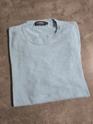Ljusblå tröja från Dressmann - Ljusblå tröja från Dressmann i mjuk bomull. Enkel design med rund halsringning och lång ärm. Perfekt för en stilren och avslappnad look.