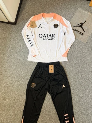 PSG träningsset Jordan x Paris - Snyggt PSG träningsset med långärmad vit tröja med persikofärgade detaljer och svart text. Hör av dig vid funderingar och behov av fler bilder! Pris går att diskuteras🤗🤗