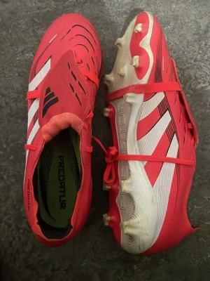 Adidas Predator röda fotbollsskor - Säljer ett par Adidas Predator fotbollsskor i rött med vita och svarta detaljer.  Snygg design med klassiska Adidas-ränder och 