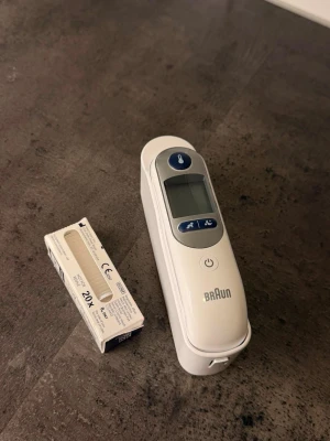 Digital febertermometer från Braun - Digital febertermometer från Braun i vit plast med blå knappar och display. Medföljer en förpackning med 20 skyddshylsor. Perfekt för att snabbt och smidigt mäta kroppstemperatur hemma.