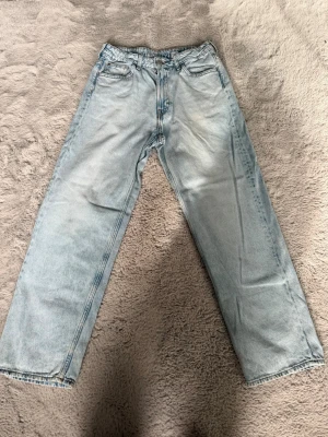 Ljusblå raka jeans från h&m - Säljer ett par ljusblå jeans med rak passform och klassisk femficksdesign. Jeansen har hög midja och är tillverkade i denim med en snygg tvättad look. Perfekta för en avslappnad och trendig stil.