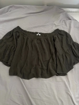 Mörkgrön offshoulder blus - Säljer en mörkgrön offshoulder blus med vida ärmar och smockad kant upptill. Blusen har en avslappnad passform och är perfekt för varma dagar. Materialet känns lätt och luftigt.