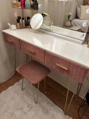 Skrivbord och sängbord i sammet - Säljer ett set med sminkbord och sängbord i rosa sammet med guldfärgade ben och handtag. Båda har vit toppskiva och lådor med dekorativa sömmar. Perfekt för att skapa en lyxig känsla i sovrummet eller sminkhörnan.