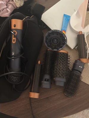 Multistyler med flera borsthuvuden - Säljer en multistyler för hår med flera utbytbara borsthuvuden och tillbehör. Setet innehåller olika borstar, rundborstar och en diffuser. Färgen är svart med kopparfärgade detaljer och allt kommer i en svart tygväska med dragkedja. Box kommer med 